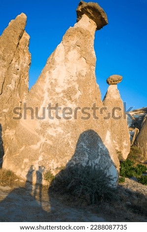 Fairy chimneys in Cappadocia, mushroom-like rocks illuminated by the evening sun with the shadow of a couple of tourists taking pictures, incredible nature of Turkey
