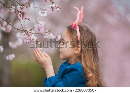 Easter. Little cute girl with long curly hair with bunny ears in cherry blossoms. Spring.