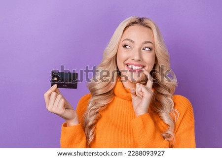 Photo of cunning tricky pretty girl with stylish hairdo dressed orange sweater look at plastic card isolated on purple color background