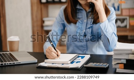 Asian business woman have the joy of talking on the smartphone and writing on the notepad in modern office 
