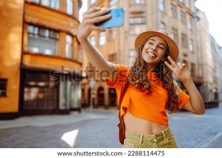Happy woman holding mobile phone takes selfie using smartphone camera. A tourist walks the streets and enjoys the architecture of the city, taking pictures of the sights. Selfie time. 