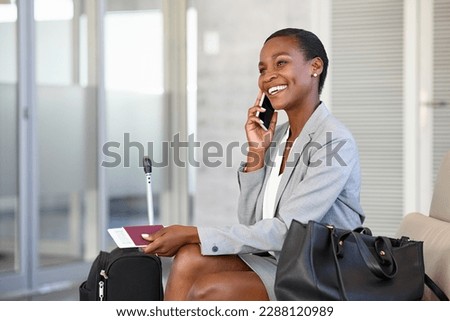 Smiling african businesswoman sitting in waiting room and talking over smartphone. Mature black woman traveller talking on cell phone at airport lounge. Successful woman on mobile phone at terminal. Royalty-Free Stock Photo #2288120989