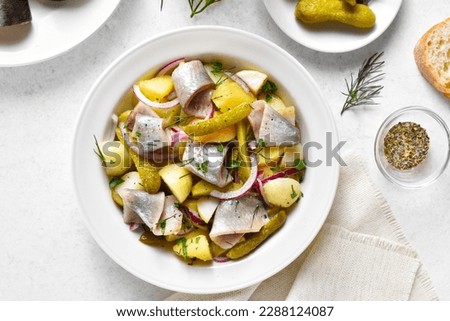 Herring salad with boiled potatoes, pickled cucumbers and red onion in bowl over white stone background. Top view, flat lay Royalty-Free Stock Photo #2288124087