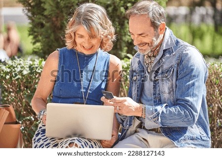 Senior Couple Enjoying Online Shopping on Laptop While Seated on Park Bench