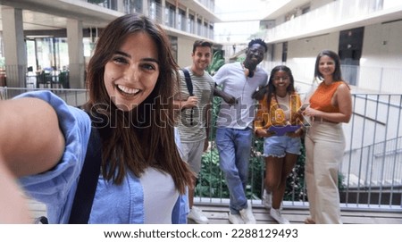 Cheerful selfie of beautiful caucasian lady at university campus gathering with multiethnic colleagues at break-time. Group of student friends taking a photo for social media.