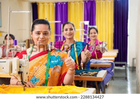 Indian woman showing thumps up while working on sewing machine at textile factory.