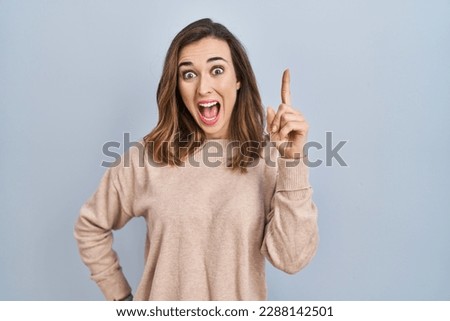 Young woman standing over isolated background pointing finger up with successful idea. exited and happy. number one. 