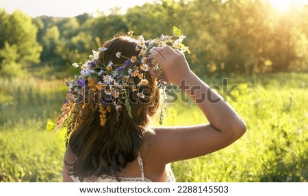 Girl in flower wreath on green sunny meadow, rear view. Floral crown, symbol of summer solstice. traditional Slavic ceremony for Midsummer, wiccan Litha sabbat. pagan folk holiday Ivan Kupala. Royalty-Free Stock Photo #2288145503
