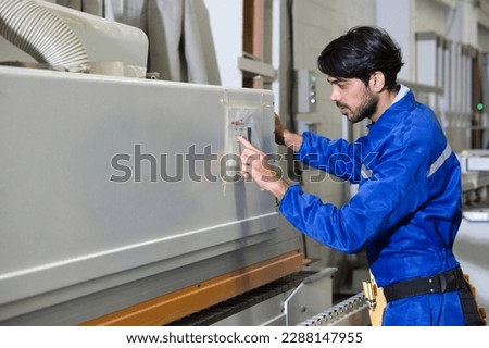 Young technician in blue mechanic jumpsuit working in furniture factory. Royalty-Free Stock Photo #2288147955
