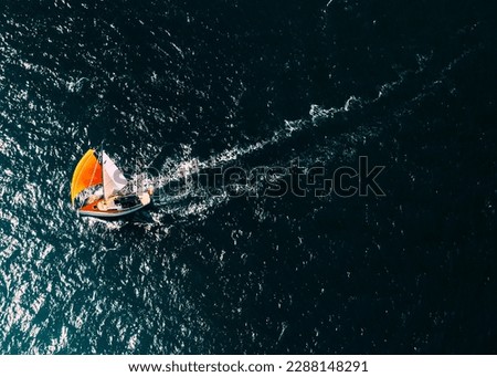 Aerial drone top down photo of a sailboat with a bright orange mast against a deep blue ocean