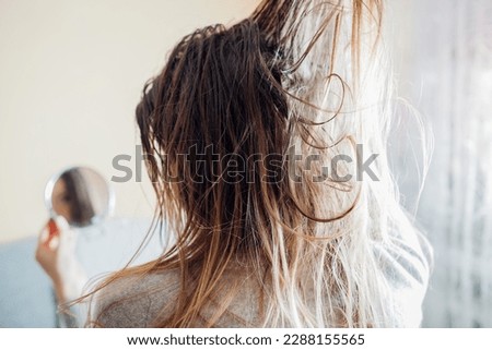 Close up of woman touching dirty oily and greasy hair looking in mirror at home. Time to wash head with high-quality shampoo. Back view Royalty-Free Stock Photo #2288155565