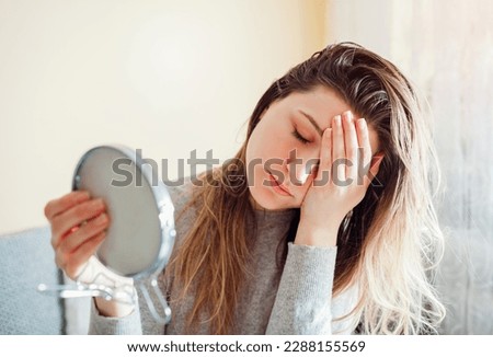 Stressed woman is sad about dirty oily and greasy hair looking in mirror at home. Healthcare. Hormonal imbalance issue Royalty-Free Stock Photo #2288155569
