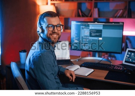 Sitting and smiling. Professional programmer is working indoors. Neon lighting. Royalty-Free Stock Photo #2288156953