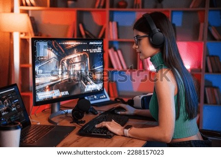 Side view. Young pretty female gamer is playing shooter. Neon lighting.