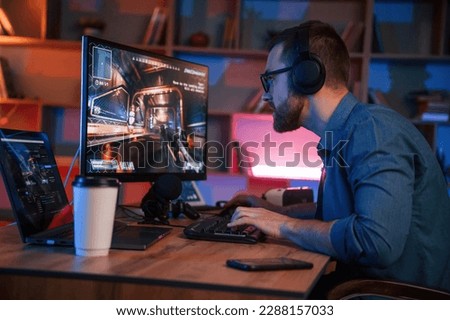 Concentrated man is playing the shooter game on his computer. Neon lighting.