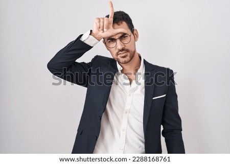 Handsome business hispanic man standing over white background making fun of people with fingers on forehead doing loser gesture mocking and insulting. 