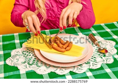 Female hands with knife and fork cutting with spaghetti and sausages or checkered green tablecloth. Dinner time. Food pop art photography. Complementary colors. Concept of food, taste, creativity