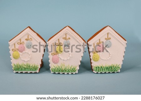Three gingerbread houses with painted eggs on them, one of which is painted with the word Easter on it.