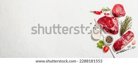 Set of various steaks with spices and herbs. Classic raw meat cuts includes ribeye, eye round and striploin steaks. Plaster white background, flat lay, banner format Royalty-Free Stock Photo #2288181553