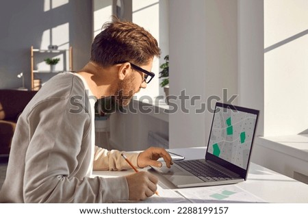 Side view portrait of professional cartographer working with cadastral map on laptop on his workplace. Young man analyzing cadastral map and searching for a building plot looking at monitor screen. Royalty-Free Stock Photo #2288199157