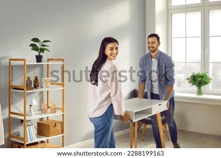 Happy family couple moving furniture at home. Joyful, positive young man and woman buy a new desk and put it in the living room in their modern apartment Royalty-Free Stock Photo #2288199163