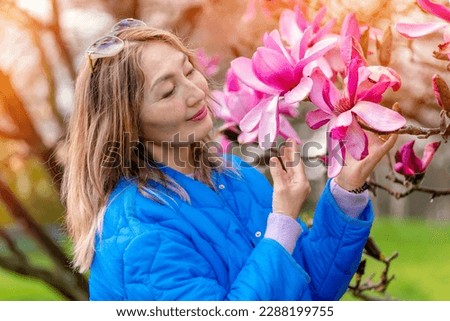Asian woman in blue coat walking in a park among flowers on spring day
