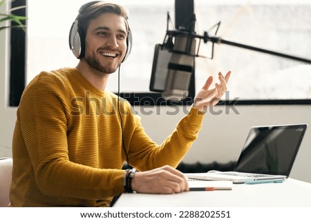 Man podcaster influencer blogger smiling while broadcasting his live audio podcast in studio using headphones, laptop and headphones. Male radio host making podcast or interview