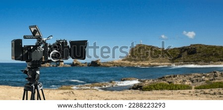 A digital movie camera films a shot on seaside. Documentary film shooting on the beach with ocean and coast background.  Royalty-Free Stock Photo #2288223293
