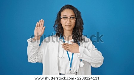 Young beautiful hispanic woman doctor making an oath with hand on chest over isolated blue wall background Royalty-Free Stock Photo #2288224111