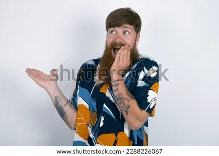 Positive Red haired man wearing printed shirt over white studio background advert promo touch finger teeth