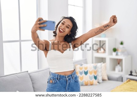 Young beautiful hispanic woman talking on smartphone standing at home
