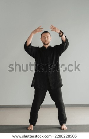 A man in black kimano practicing qigong energy exercises indoors. Royalty-Free Stock Photo #2288228505