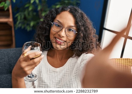 Young latin woman drinking champagne making selfie by the camera at home
