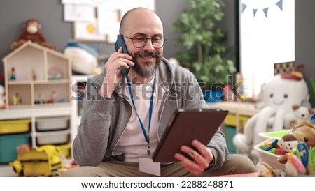 Young bald man preschool teacher using touchpad speaking on the phone at kindergarten Royalty-Free Stock Photo #2288248871