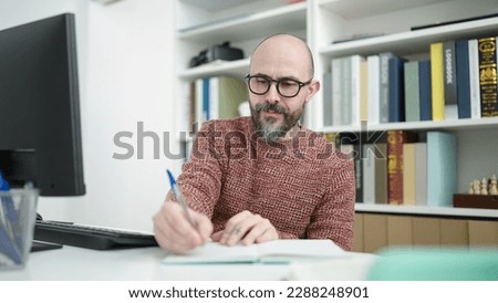 Young bald man student using computer writing on notebook at university classroom