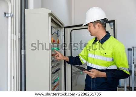 An engineer or electrician working push button on electrical system of water supply system controller with tablet at factory. Royalty-Free Stock Photo #2288251735