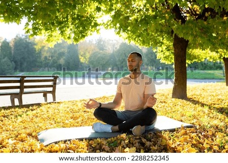 A young Latin American man is doing yoga in the morning in the park. Sitting on a mat in the lotus position with closed eyes and meditating. Royalty-Free Stock Photo #2288252345