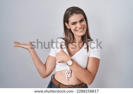 Young beautiful woman wearing casual white t shirt showing palm hand and doing ok gesture with thumbs up, smiling happy and cheerful 