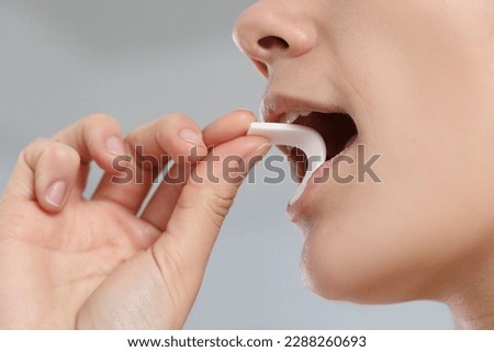 Woman putting chewing gum into mouth on blurred background, closeup Royalty-Free Stock Photo #2288260693
