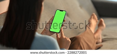 Young woman home use green screen mockup Smartphone, her sitting on sofa in living room
