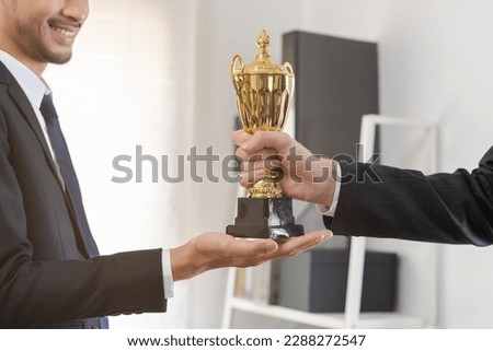 Good job of achievement, happy success asian young businessman, man employee holding golden trophy cup, team getting rewarded for winning from caucasian man boss. Celebration of Teamwork of business. Royalty-Free Stock Photo #2288272547