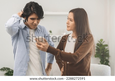 Infidelity, suspicion asian young couple love fight relationship, wife holding cellphone, smartphone cheating on phone, scolding husband about mistrust, distrust and jealousy when sitting at home. Royalty-Free Stock Photo #2288272591