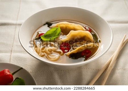 Gyoza miso soup with dumplings in white bowl, bright background