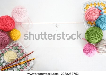 multicolored woolen balls with granny sqaure and crochet hook on white wooden ground with space for text handmade