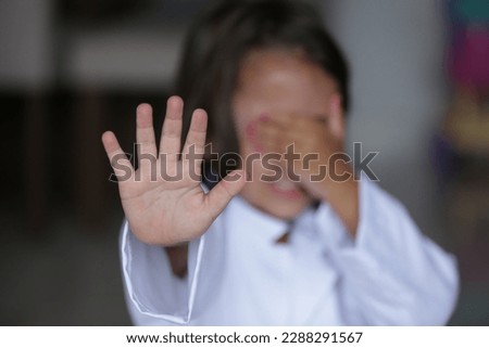 Child with hand on face signaling stop with other hand.