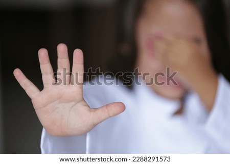 Child with hand on face signaling stop with other hand.