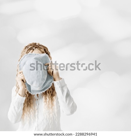 Creative summer visual. Aesthetic vacation and holiday concept, woman holding sun hat in front of face, no face trend concept. Stylish female with long hair hiding behind blue panama, summer lifestyle
