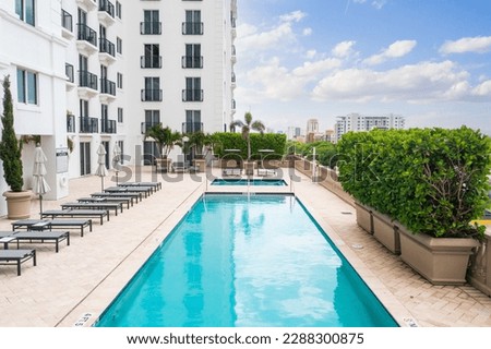 Point of view of the pool, in a hotel with several lounge chairs and umbrellas around, spa, balconies, windows, privet, palms and plants around