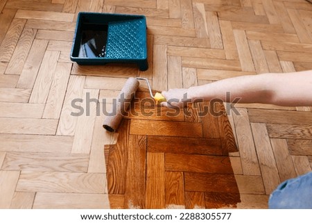 man varnishes oak parquet with a roller during renovation Royalty-Free Stock Photo #2288305577