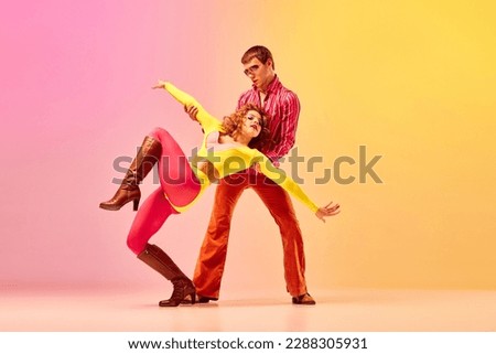 Emotions in movemets. Young stylish emotional man and woman, professional dancers in retro style clothes dancing disco dance over pink-yellow background. 1970s, 1980s fashion, music concept Royalty-Free Stock Photo #2288305931